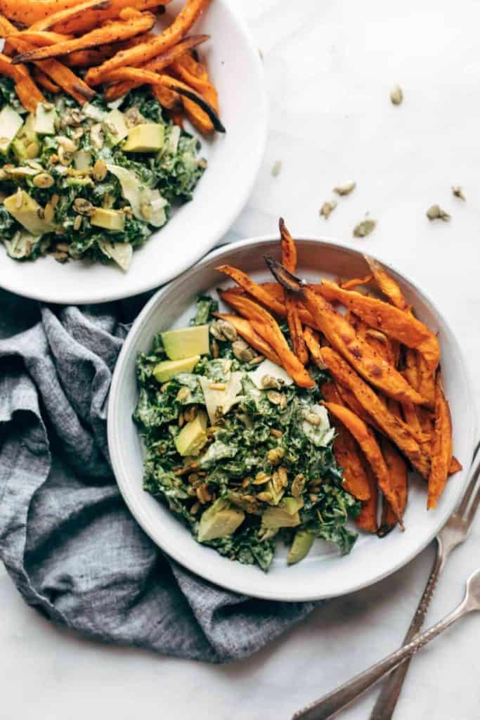 a photo of a kale salad with sweet potato fries. 